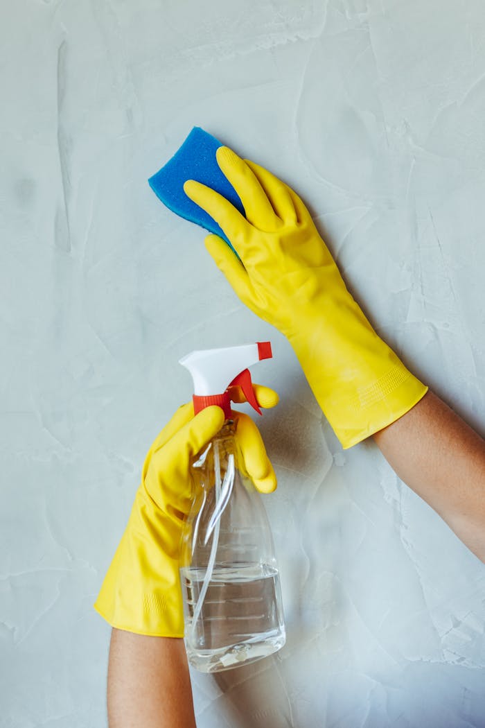 testimonials-img Hands in yellow gloves cleaning wall with sponge and spray bottle.